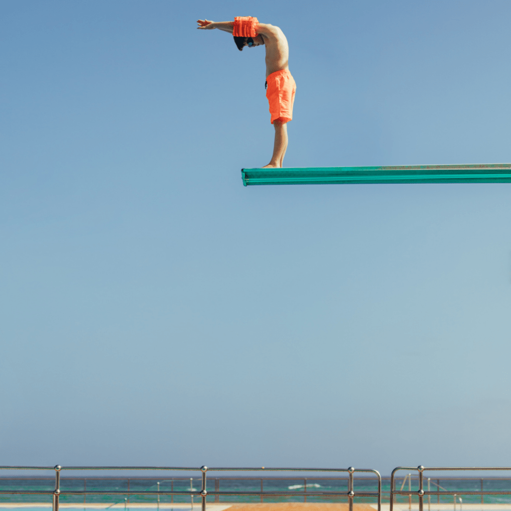 Hotel Content Marketing für einen professionellen Markenauftritt.
Auf dem Bild sieht man einen jungen in orange-farbener Badehose und orangenen Schwimmflügeln. Der Junge steht auf einem Sprungbrett, bereit in das Schwimmbecken zu springen. Im Hintergrund sieht man ein Meer.